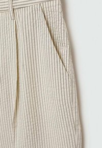 Pantalones de tela color crema con rayas verticales en azul marino, que cuentan con bolsillos laterales y un acabado texturizado. El diseño enfatiza líneas limpias y un ajuste a medida.