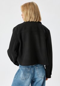 Schwarze, taillierte Jacke mit einem figurschmeichelnden Design, gefertigt aus einem weichen, strukturierten Stoff. Besitzt weite Ärmel und einen schlichten, nahtlosen Rücken.