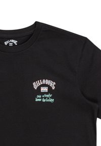 Sort t-shirt med korte ærmer, prydet med et farverigt trykt logo og tekst: "BILLABONG" øverst og "Kun en surfer kender følelsen" nedenfor.