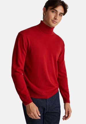 Jersey de cuello alto ajustado en rojo, hecho de una suave tela de punto, con mangas largas y detalles acanalados en el cuello y los puños. Combinado con jeans oscuros.