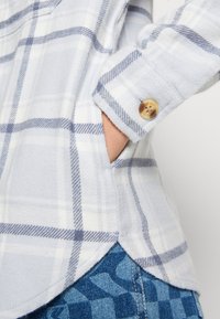 Ljusblå rutig skjorta i mjukt tyg, med vita och marinblå ränder, knappade ärmslut och rundad nederkant, med en synlig framficka.