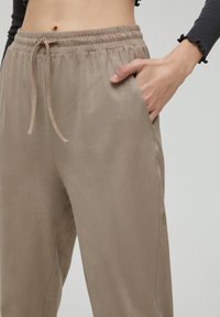 En närbild av en person som bär beige sweatpants med elastisk midja och en hand i fickan, vilket visar en avslappnad stil.