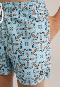 Vieglas auduma peldbikses gaiši zilā krāsā, ar atkārtotu tumši zilu un oranžu lapu rakstu. Elastīga josta ar auklu.