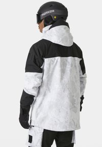 Chaqueta de esquí con un patrón de camuflaje en blanco y negro, que cuenta con capucha, mangas largas y acentos de velcro en los puños y bolsillos.