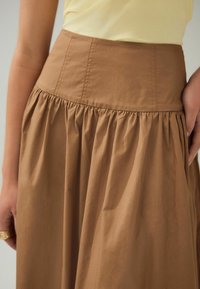 Jupe en coton marron avec une taille ajustée et une texture froncée. Présente des détails de couture subtils le long de la taille et un design fluide et plissé.