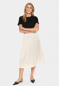 Svart tajt t-shirt, krämfärgad satin midi-kjol, slät textur, ankle-length, kombinerat med svarta spetstångade ballerina med rosettdetalj.