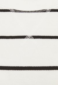 Jersey blanco con rayas horizontales negras, con una textura de punto y detalle de costura visible en el escote.