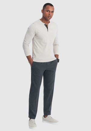 Camisa henley de manga larga gris claro con tapeta y botones negros, combinada con pantalones gris oscuro y zapatillas ligeras.