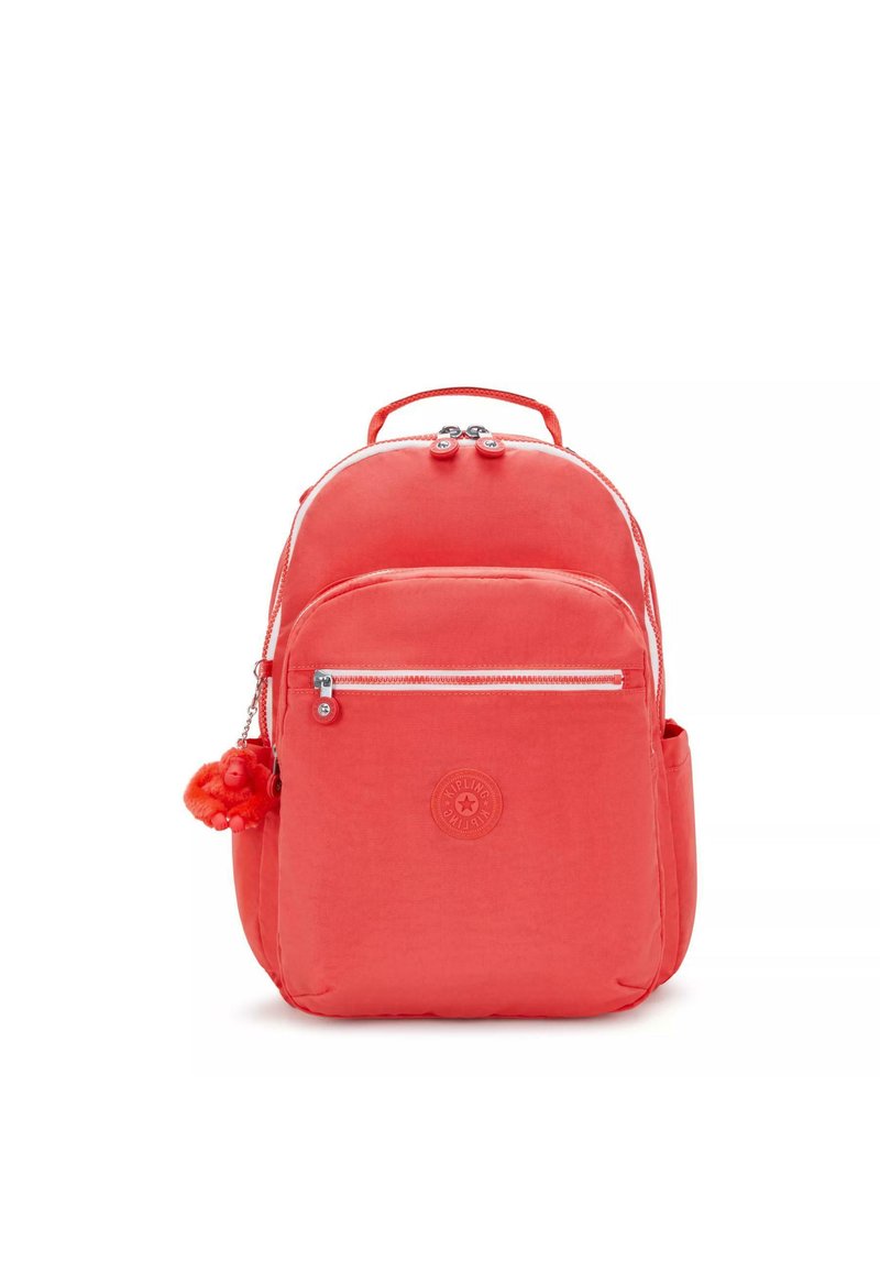 Mochila coral con material de nailon, dos compartimentos con cremallera, un llavero decorativo con pompón y un logotipo circular en la parte frontal.