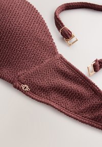 Close-up of a textured maroon bikini top with gold adjustable strap buckles and a small round gold charm attached.