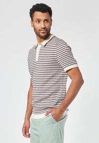 Neulepolo, jossa on vaakaraitoja kerma, burgundy ja laivastonsininen; pehmeä kangas, klassinen kaulus ja ribattu reunus.