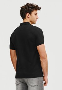 Czarna koszulka polo z materiału bawełnianego, z klasycznym kołnierzykiem i krótkimi rękawami. Zaprojektowana w slim fit z gładką teksturą.