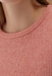 Ljusrosa stickad tröja med ribbat mönster, med en bred rund halsringning. Mjukt material med subtil lyster och detaljer.