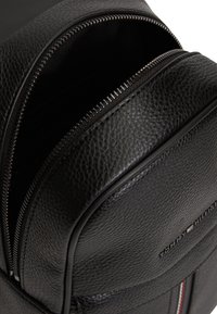 Μαύρο δερμάτινο σακίδιο πλάτης με υφή, που διαθέτει ομαλό φερμουάρ και λεπτομέρεια με λογότυπο. Το εσωτερικό προσφέρει άφθονο αποθηκευτικό χώρο.