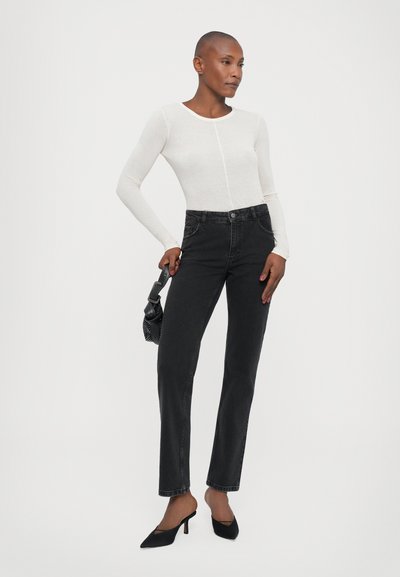 White long-sleeve top and high-waisted black jeans. The jeans are straight-cut with minimal detailing. Black pointed-toe heels and a small bag.