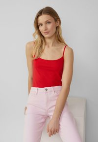 Rode, getailleerde tanktop met dunne bandjes, gecombineerd met lichtroze jeans. Gladde stoftextuur met een eenvoudig, strak ontwerp.