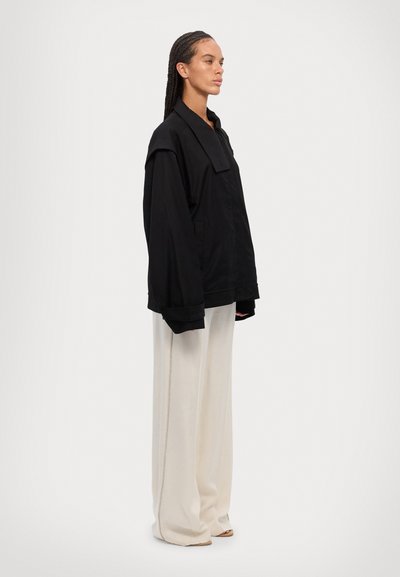 Chaqueta negra de gran tamaño con un cuello estructurado, que presenta un corte relajado, combinada con pantalones de pierna ancha crema de tiro alto.