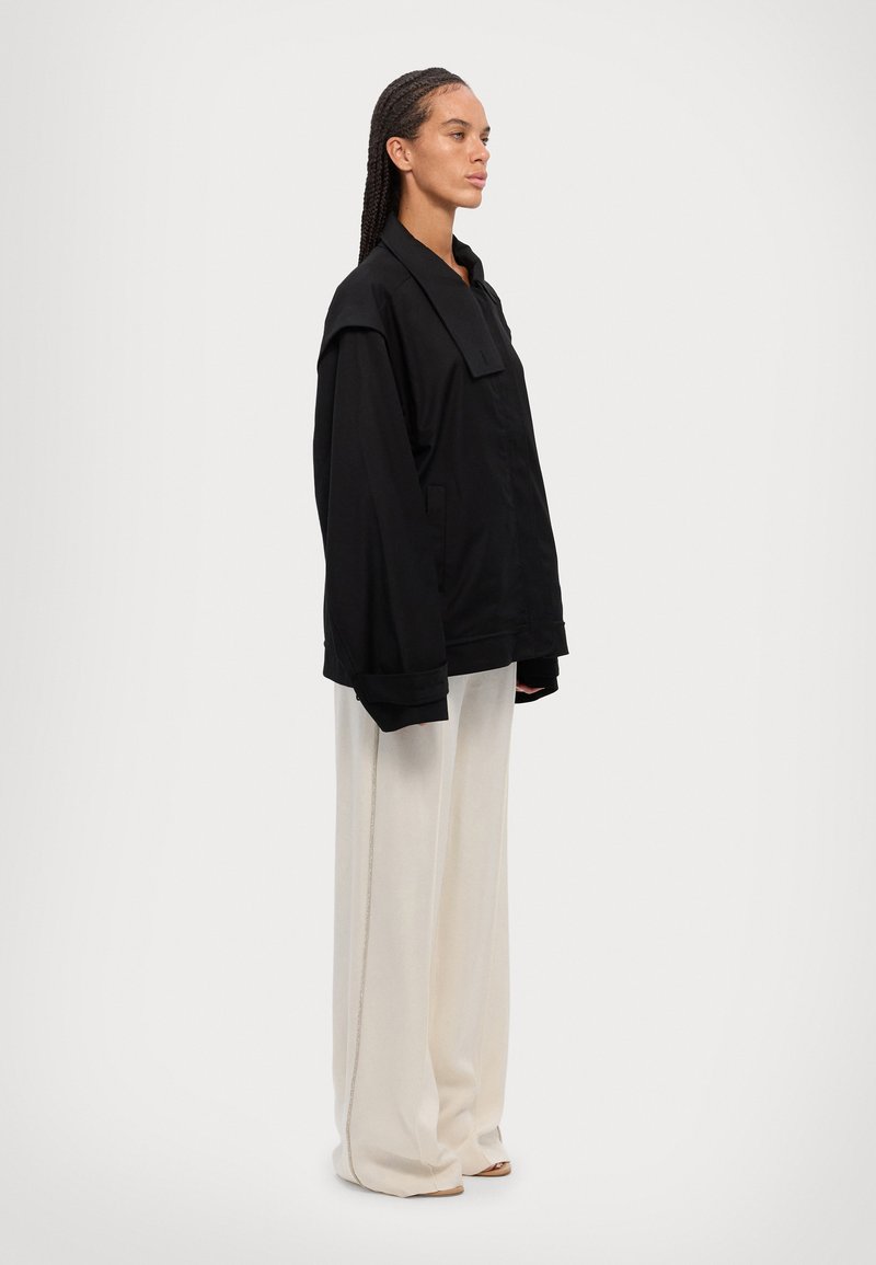 Black oversized jacket with a structured collar, featuring a relaxed fit, and paired with high-waisted, cream wide-leg pants.