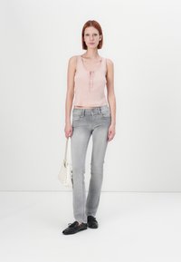Lyserosa ribbet topp med blonder, parret med lysegrå tettsittende jeans. Modellen holder en liten hvit håndveske, iført svarte sko.