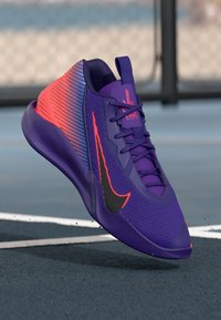 Purple athletic shoe with gradient design transitioning to pink, featuring a black Nike swoosh, textured upper, and cushioned sole.