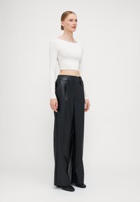 White long-sleeve cropped top paired with high-waisted, wide-leg black faux leather trousers featuring two belt loops. Smooth texture overall.