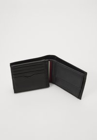Portafoglio in pelle nera aperto per mostrare diversi slot per carte, un interno liscio e un sottile accento rosso. Presenta un logo del marchio impresso all'interno.