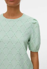 Top verde menta con un motivo testurizzato di diamanti e accenti floreali, con maniche corte e puffate e scollatura rotonda.