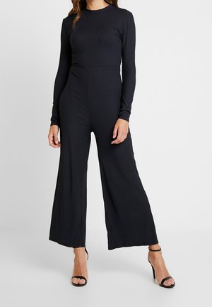 Combinaison noire côtelée à manches longues, haut ajusté et pantalons à jambes larges. Comprend un col rond et un motif texturé subtil.