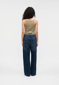 Φωτεινό ελαιώδες αμάνικο τοπ συνδυασμένο με φαρδιά τζιν παντελόνια σε σκούρο μπλε χρώμα. Το τζιν έχει ψηλή μέση και δύο τσέπες πίσω.