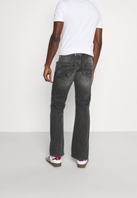 Vaqueros de mezclilla gris con un corte relajado, que cuentan con bolsillos traseros distintivos y un ligero desvanecimiento. Combinados con una camiseta blanca lisa y zapatos informales.