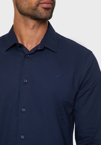 Donkerblauwe overhemd met lange mouwen en knopen, gemaakt van gladde stof, met een puntige kraag, subtiele geborduurde logo en bijpassende knopen.