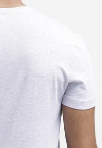 Camiseta de cuello redondo en gris claro, con mangas cortas, fabricada en una tela suave. Presenta una textura lisa y un diseño simple, sin adornos.