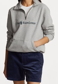 Světle šedá mikina na zip s vysokým límcem a přední kapsou, se tmavě zeleným logem "Polo Ralph Lauren". Námořnické manšestrové šortky.