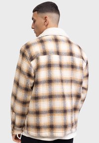 Fleecejacke mit einem braun-gelben Karomuster, einem weißen Lammfellkragen und einer lockeren Passform mit geknöpften Manschetten.