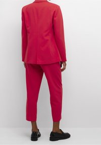 Felroze pak met een nauwsluitend colbert en korte broek. Gemaakt van gladde stof, met een eenvoudig ontwerp en minimalistische details. Zwarte schoenen.