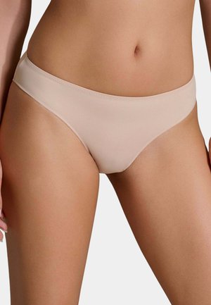 Donna che indossa biancheria intima stile bikini liscia, color carne, mostrando l'area addominale e la parte superiore delle cosce su uno sfondo semplice.