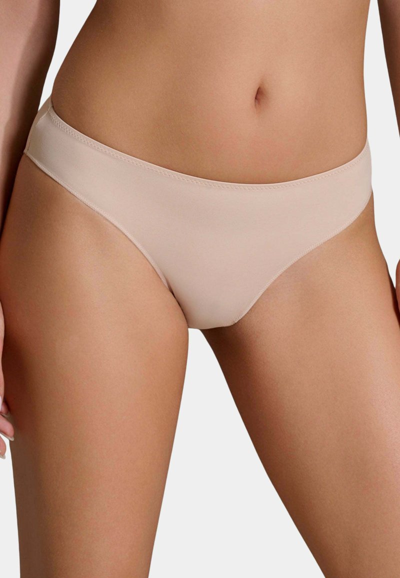 Donna che indossa biancheria intima stile bikini liscia, color carne, mostrando l'area addominale e la parte superiore delle cosce su uno sfondo semplice.