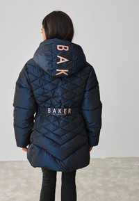 Marineblauwe gewatteerde jas met ruitsteek, grote capuchon en logo "BAKER" in lichtroze op de achterkant, getailleerde taille voor een mooie vorm.