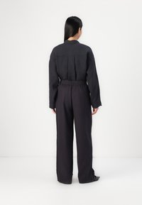 Black linen top with long sleeves and back pleat, paired with wide-leg black trousers featuring an elastic waistband.