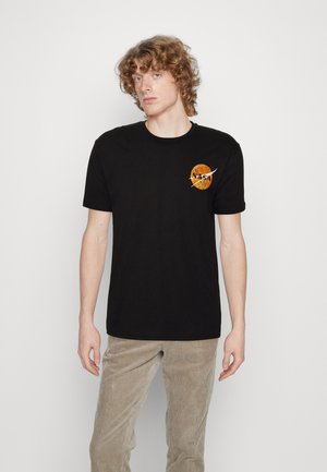 T-shirt nera in cotone con un logo NASA arrotondato in arancione e giallo sul lato sinistro del petto. Maniche corte e scollo rotondo.