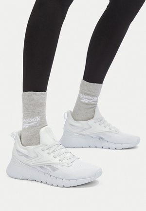 Beine in schwarzen Leggings, grauen Reebok-Socken und weißen Reebok-Sportschuhen mit Mesh und gepolsterten Sohlen.
