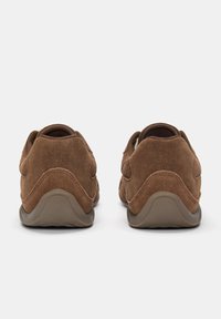 Scarpe slip-on in suede marrone con tacco arrotondato, upper testurizzato e dettagli di cucitura visibili. Fodera morbida visibile all'apertura.