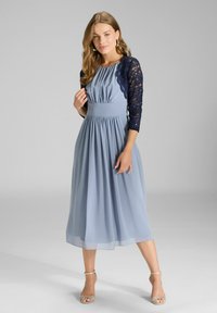 Sukienka o długości midi w jasnoniebieskim szyfonie z plisowanym korpusem i granatowymi koronkowymi rękawami 3/4. Połączona z sandałami na przezroczystym obcasie.