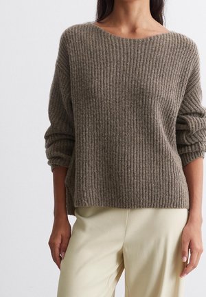 Pull en maille côtelée marron avec un large décolleté et des épaules tombantes, associé à un pantalon crème en tissu doux et texturé.