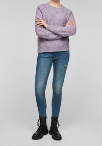 Jasnofioletowy dzianinowy sweter z fakturowanym wzorem, zestawiony z ciemnoniebieskimi obcisłymi jeansami i czarnymi skórzanymi butami wojskowymi na sznurowadła.