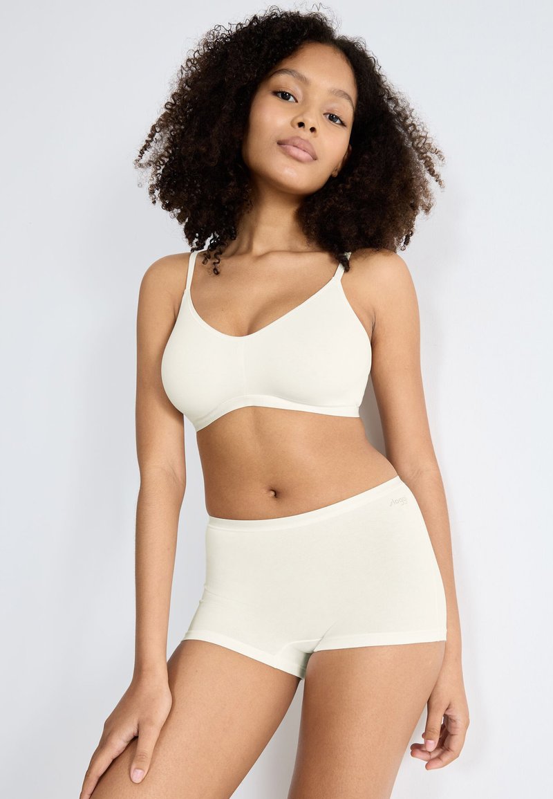 Sujetador de tela suave en color crema claro con tirantes ajustables, combinado con pantalones cortos de cintura alta a juego, que presentan costuras mínimas y un ajuste ceñido.