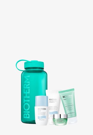 Transparente, türkisfarbene Wasserflasche mit Schraubverschluss, neben drei Pflegeprodukten in weißen und hellgrünen Tuben und Töpfen.