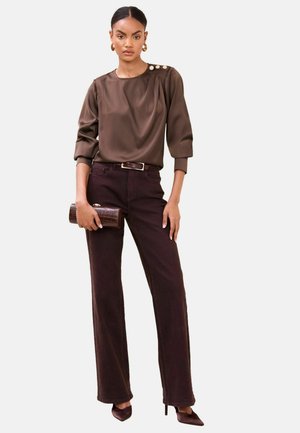 Brown satin blouse with three-quarter sleeves and button details on the shoulder, paired with high-waisted chocolate trousers and matching heels.