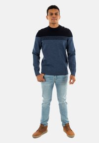 Maglione a maglia blu e navy con una fascia testurizzata sul petto, abbinato a jeansazzurri chiari e stivali marroni con lacci.