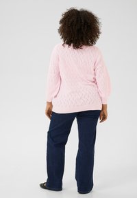 Pull en tricot rose avec un motif en losanges texturé, coupe décontractée et poignets côtelés, assorti à un jean droit bleu foncé.